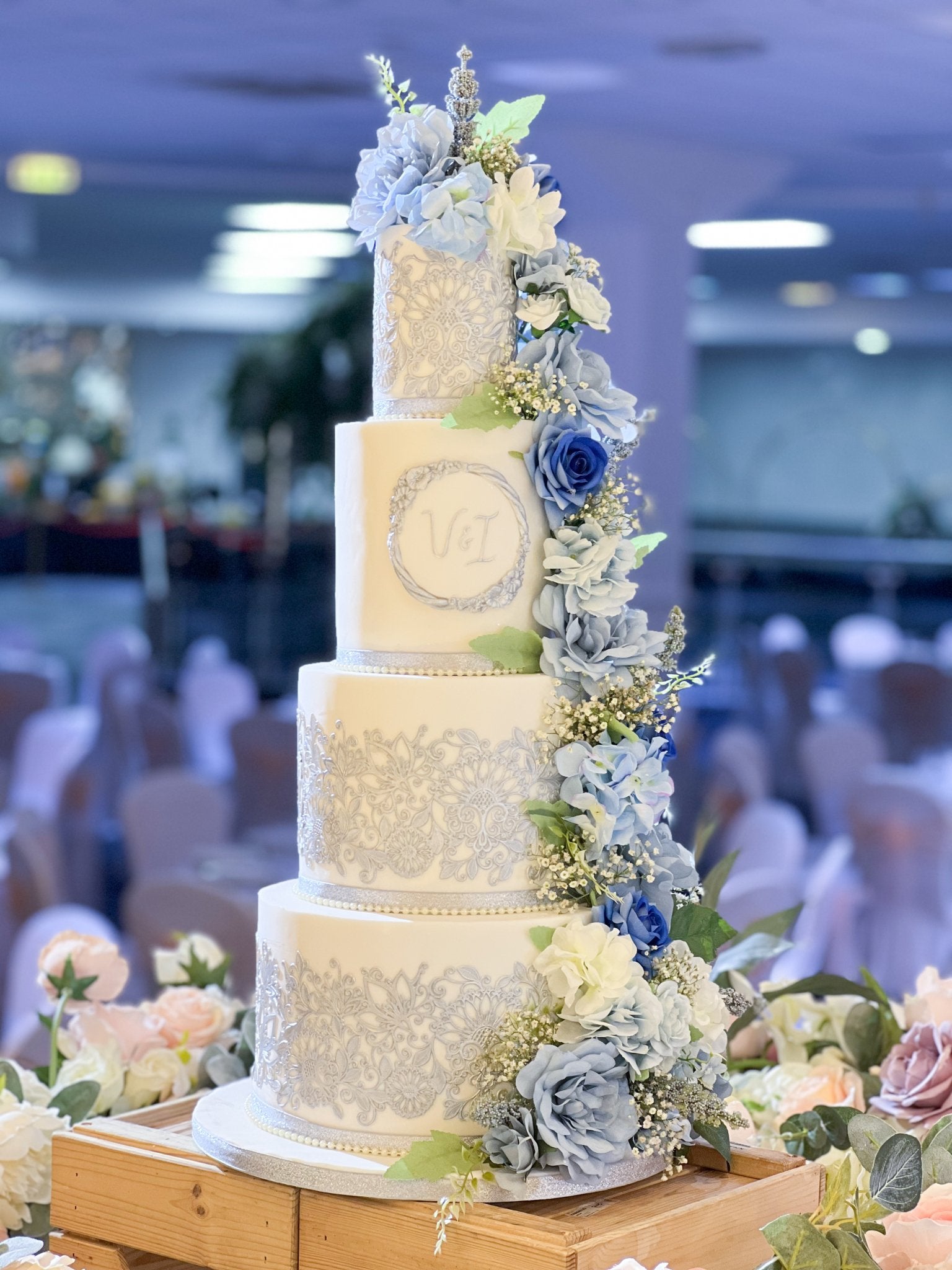Four-tier silver and blue floral wedding cake with intricate decorations.