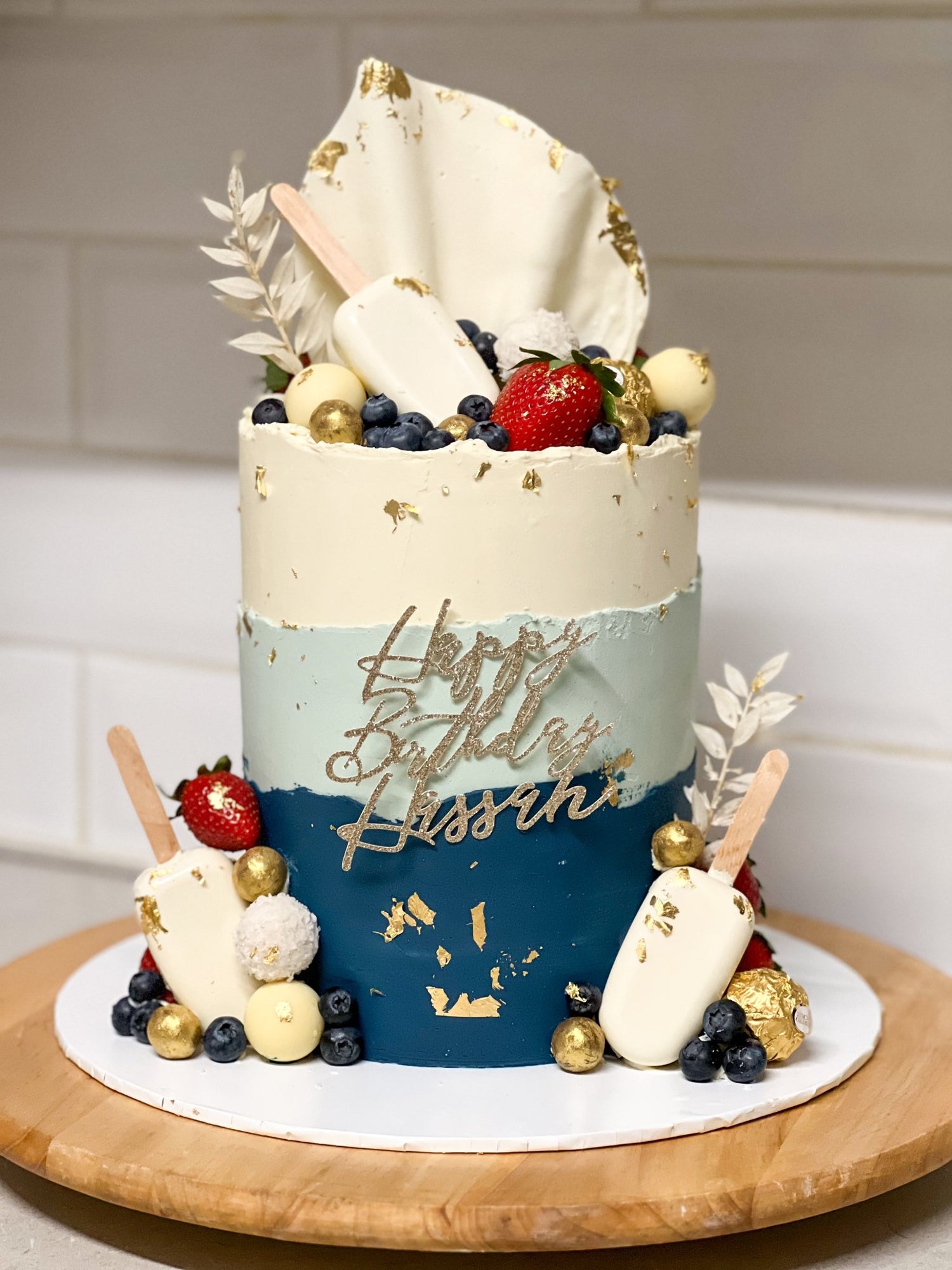 Blue and gold celebration cake topped with fresh strawberries.